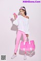 A woman in a white sweatshirt and pink leggings holding a pink bag.