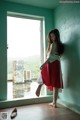 A woman in a red dress standing in front of a window.