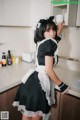 A woman in a maid outfit standing in a kitchen.