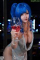 A woman with blue hair holding a glass of wine.