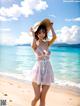 A woman in a white dress and hat standing on a beach.