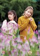 A couple of women standing next to each other in a field of flowers.