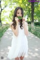 A young woman in a white dress holding a leaf in her mouth.